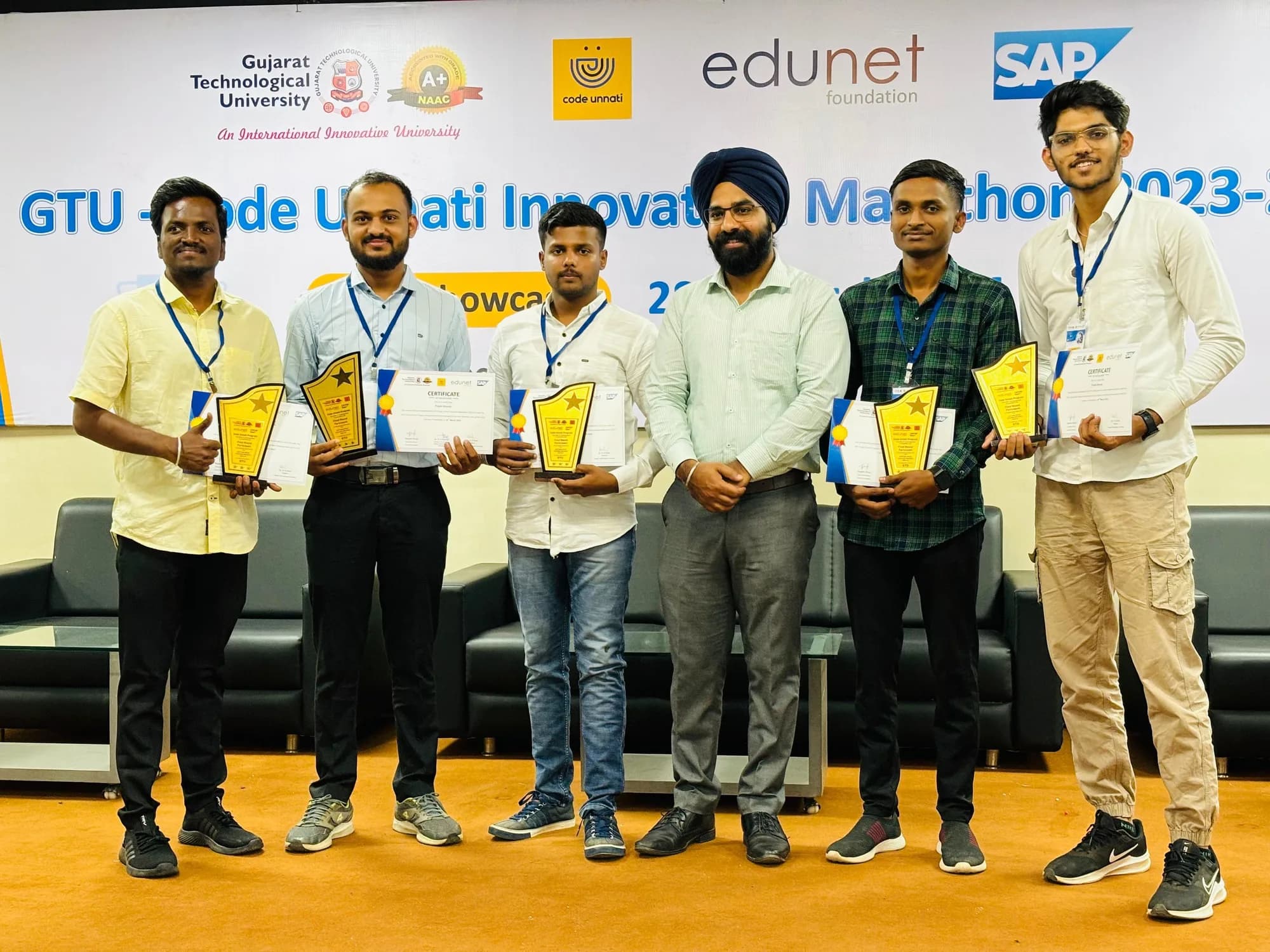 Participants holding trophies and certificates on stage at the GTU–Code Unnati Innovation Marathon 2023-24 final showcase.