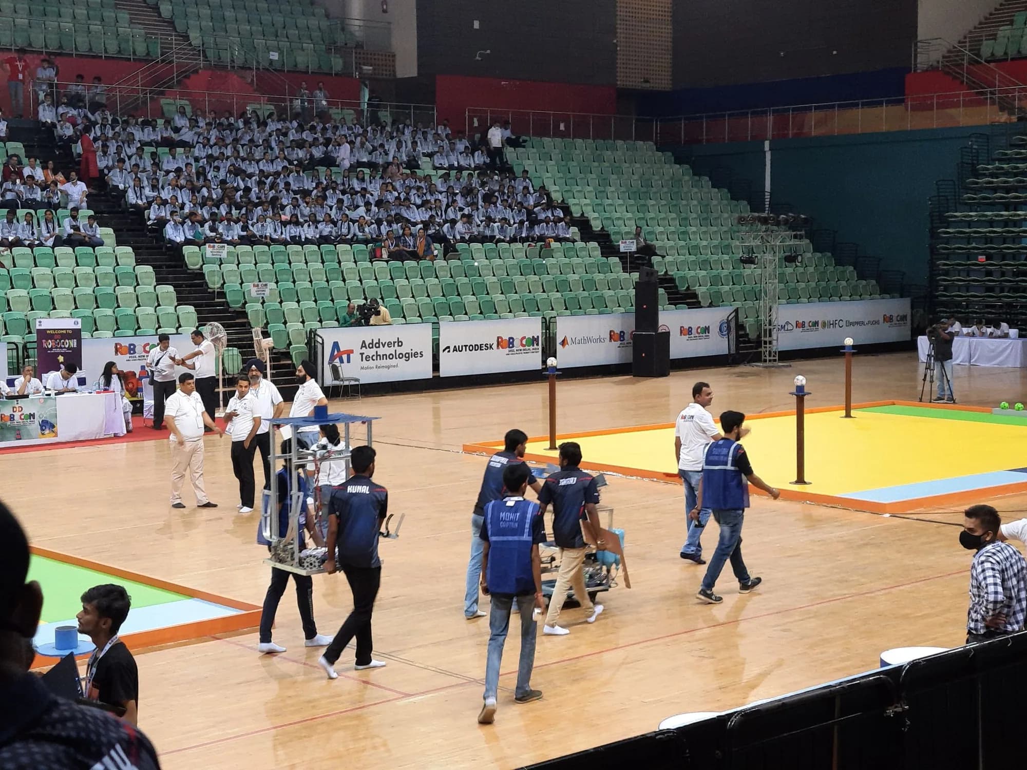 Teams carrying their robots onto the DD Robocon 2022 contest floor in New Delhi, with the crowd seated in the stands.
